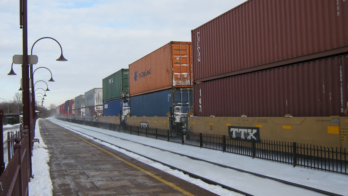Double-stacked shipping containers on a freight train passing a snowy railway platform.